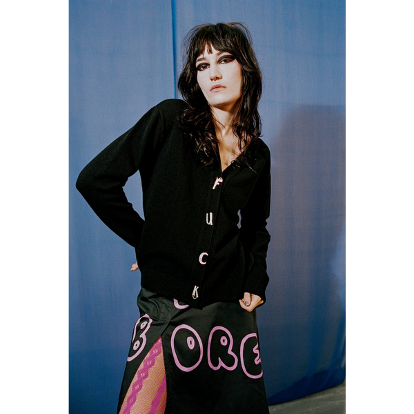 Person wearing a black cardigan and colourful skirt with 'BORED' text against a blue background