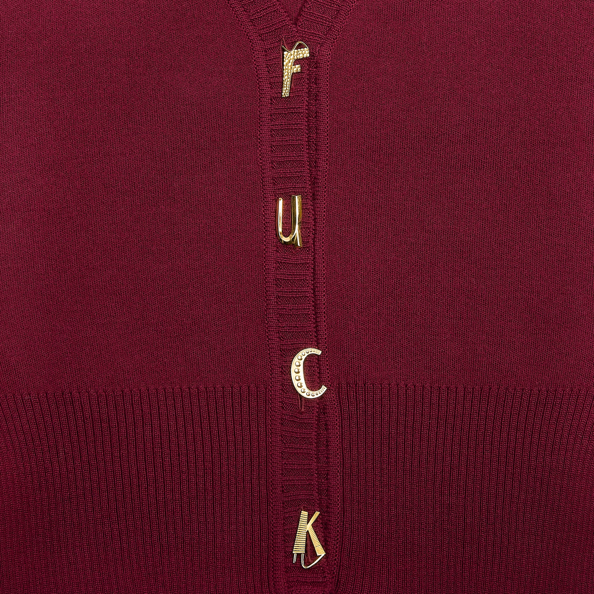 Close-up of a maroon knit cardigan featuring gold-tone letter charms spelling 'F**K' down the centre of the chest.