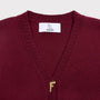 Close-up of a maroon knit cardgian with a white HADES neck label and a small gold embroidered letter F at the center of the chest.