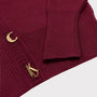Close-up of a maroon ribbed knit cardigan with gold-tone decorative buttons, including stylized letter designs, on a light gray background.