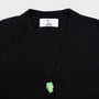 Close-up of a black knit cardigan with a white HADES brand label at the collar and a small mint green sculptural button at the center of the V.