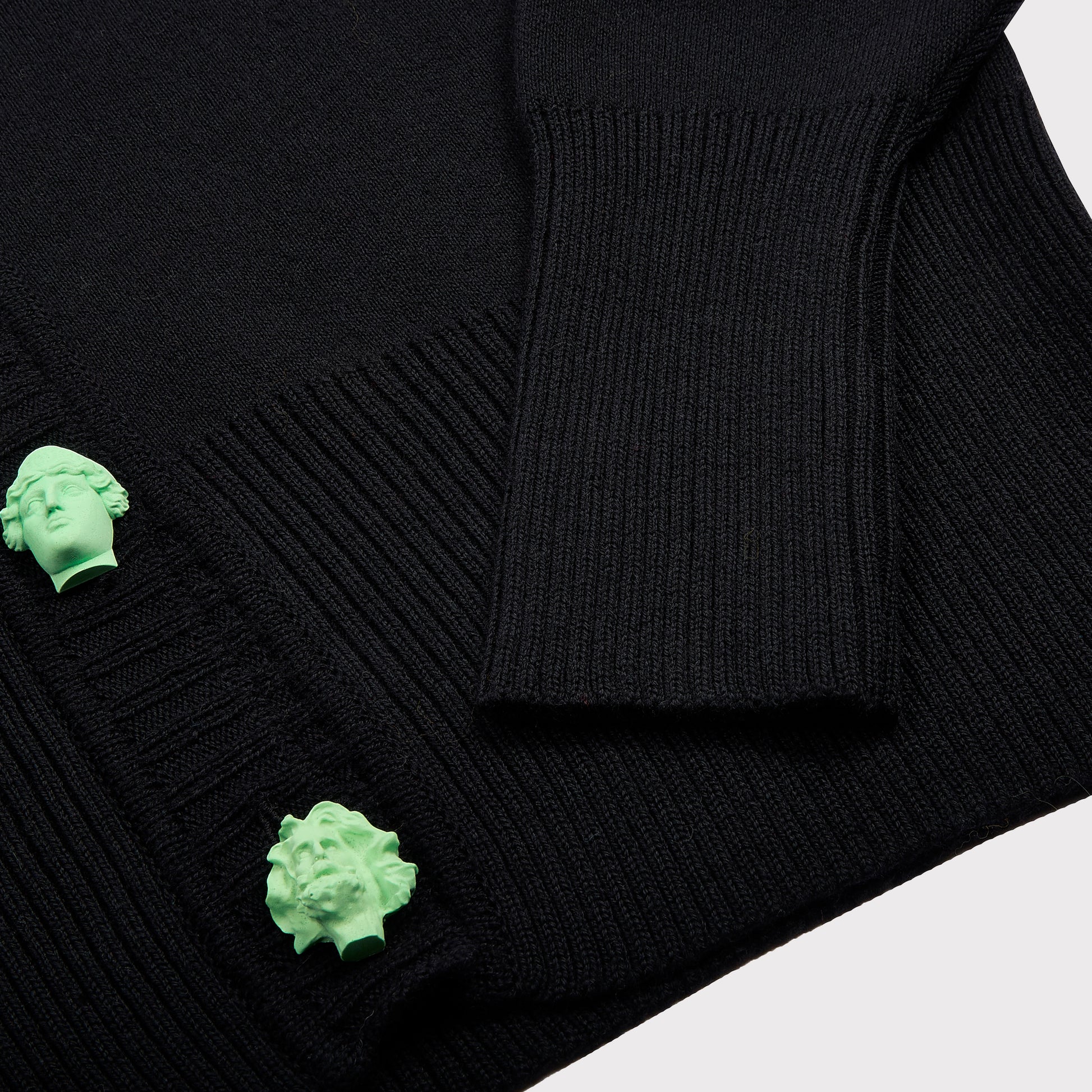 Close-up of a black ribbed knitc ardigan featuring two bright mint green sculptural Greek Mythology buttons.