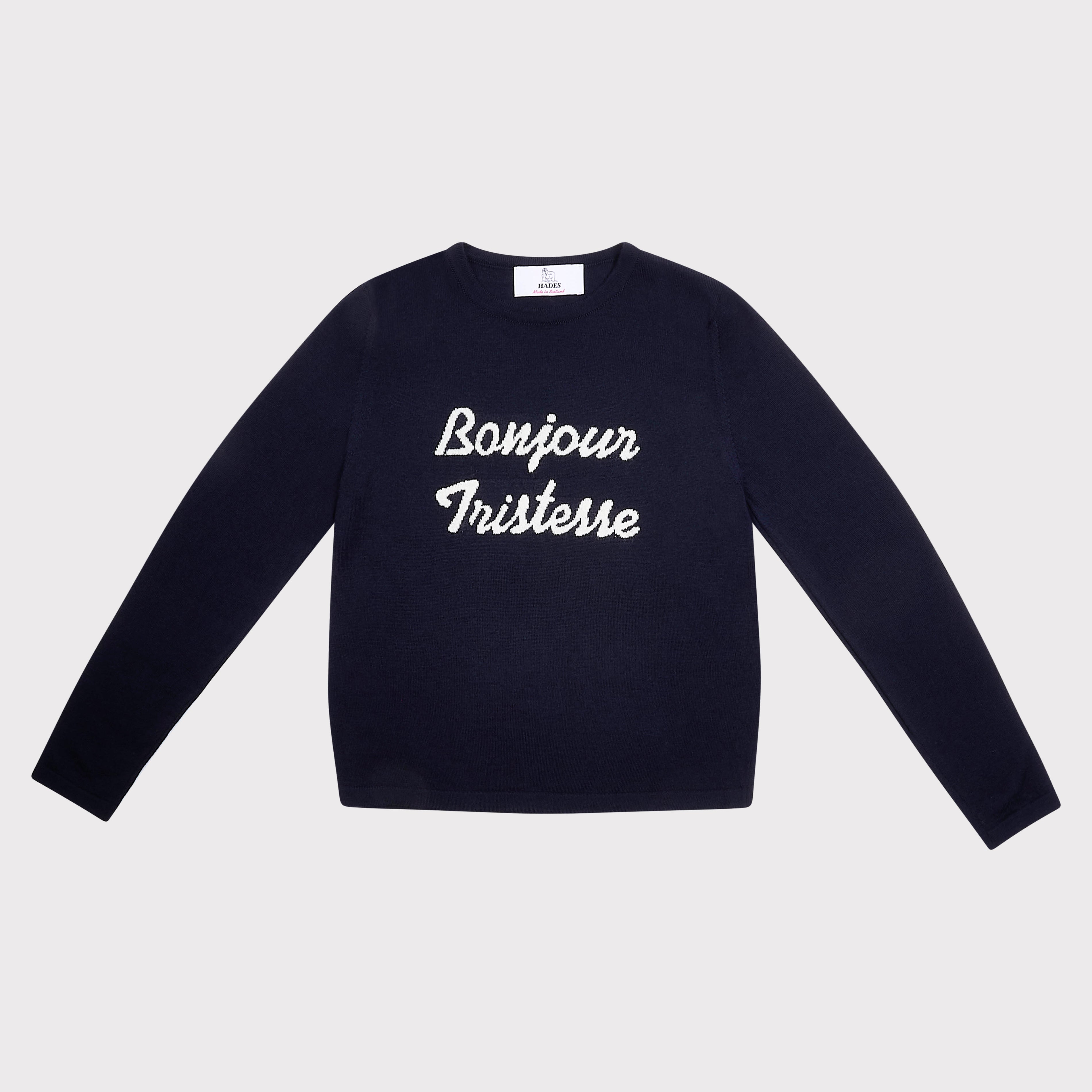 A navy blue long-sleeve crewneck sweatshirt with 'Bonjour Tristesse' printed in white script across the chest, displayed flat against a light gray background.
