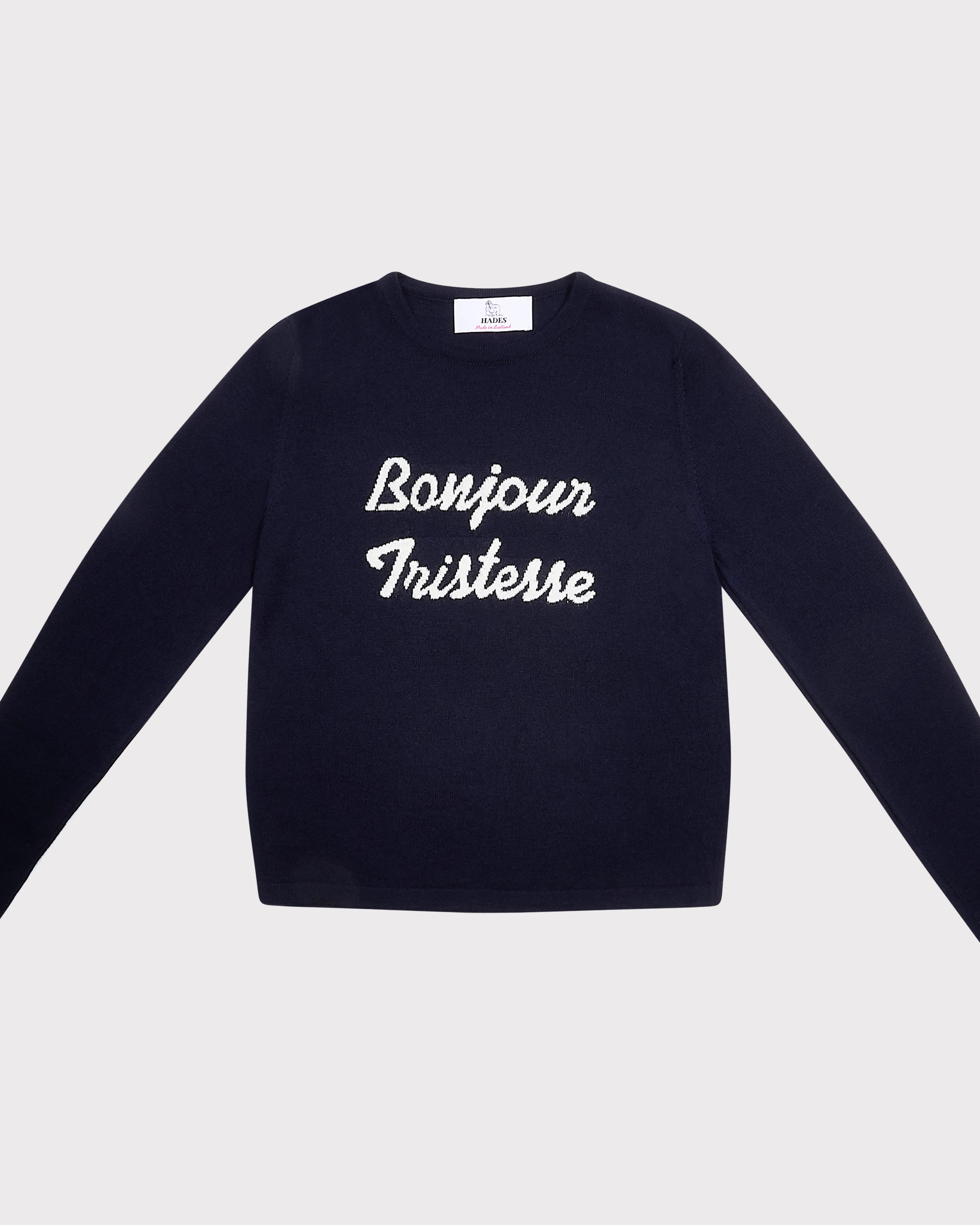 A navy blue long-sleeve crewneck sweatshirt with 'Bonjour Tristesse' printed in white script across the chest, displayed flat against a light gray background.