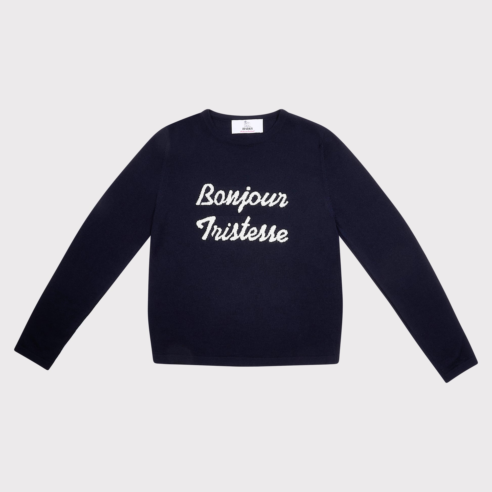 A navy blue long-sleeve crewneck sweatshirt with 'Bonjour Tristesse' printed in white script across the chest, displayed flat against a light gray background.
