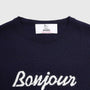 Close-up of a navy blue knit sweater with 'Bonjour Tristesse' knitted in white script across the chest.