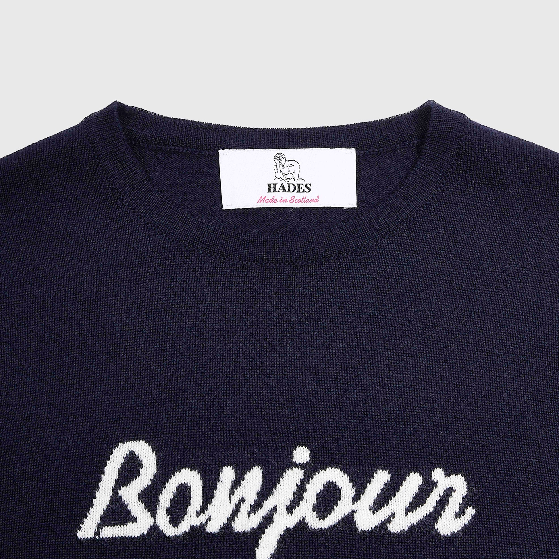Close-up of a navy blue knit sweater with 'Bonjour Tristesse' knitted in white script across the chest.