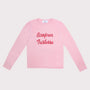 A light pink long-sleeve crewneck shirt with 'Bonjour Tristesse' printed in red cursive across the chest, displayed flat against a light gray background.