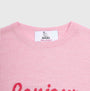 Close-up of a light pink knit crewneck sweater with a white neck label reading HADES Made in Scotland.