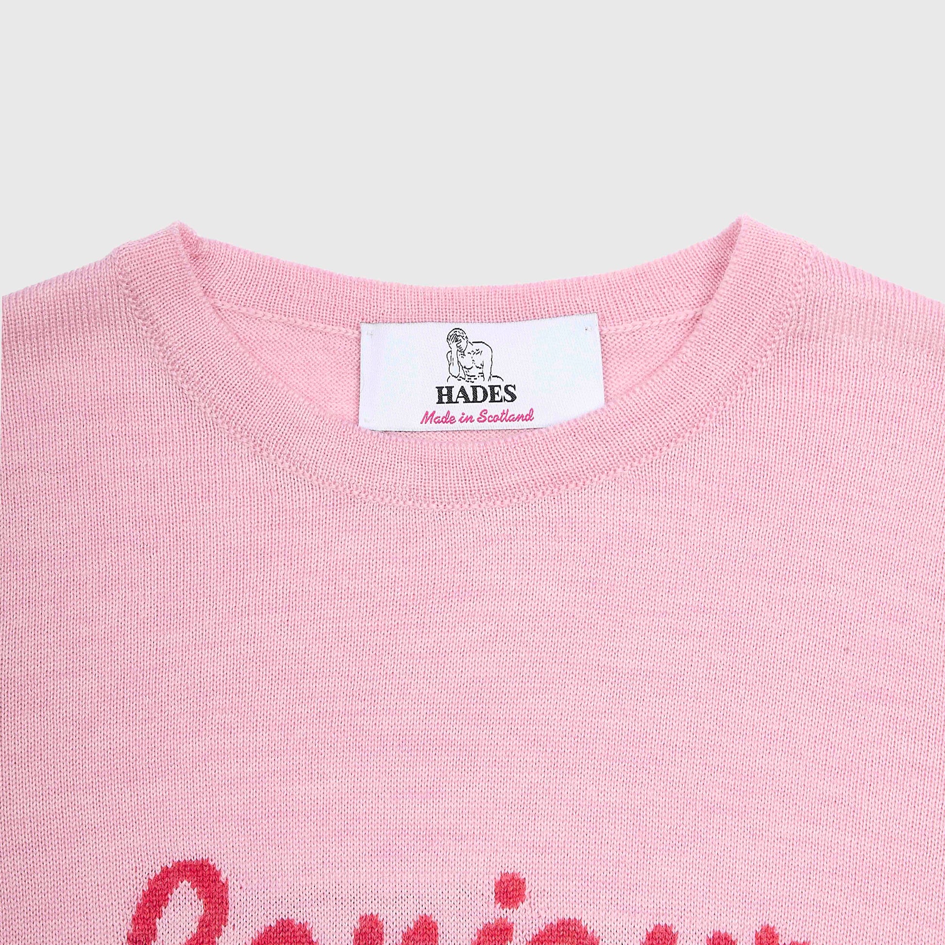 Close-up of a light pink knit crewneck sweater with a white neck label reading HADES Made in Scotland.