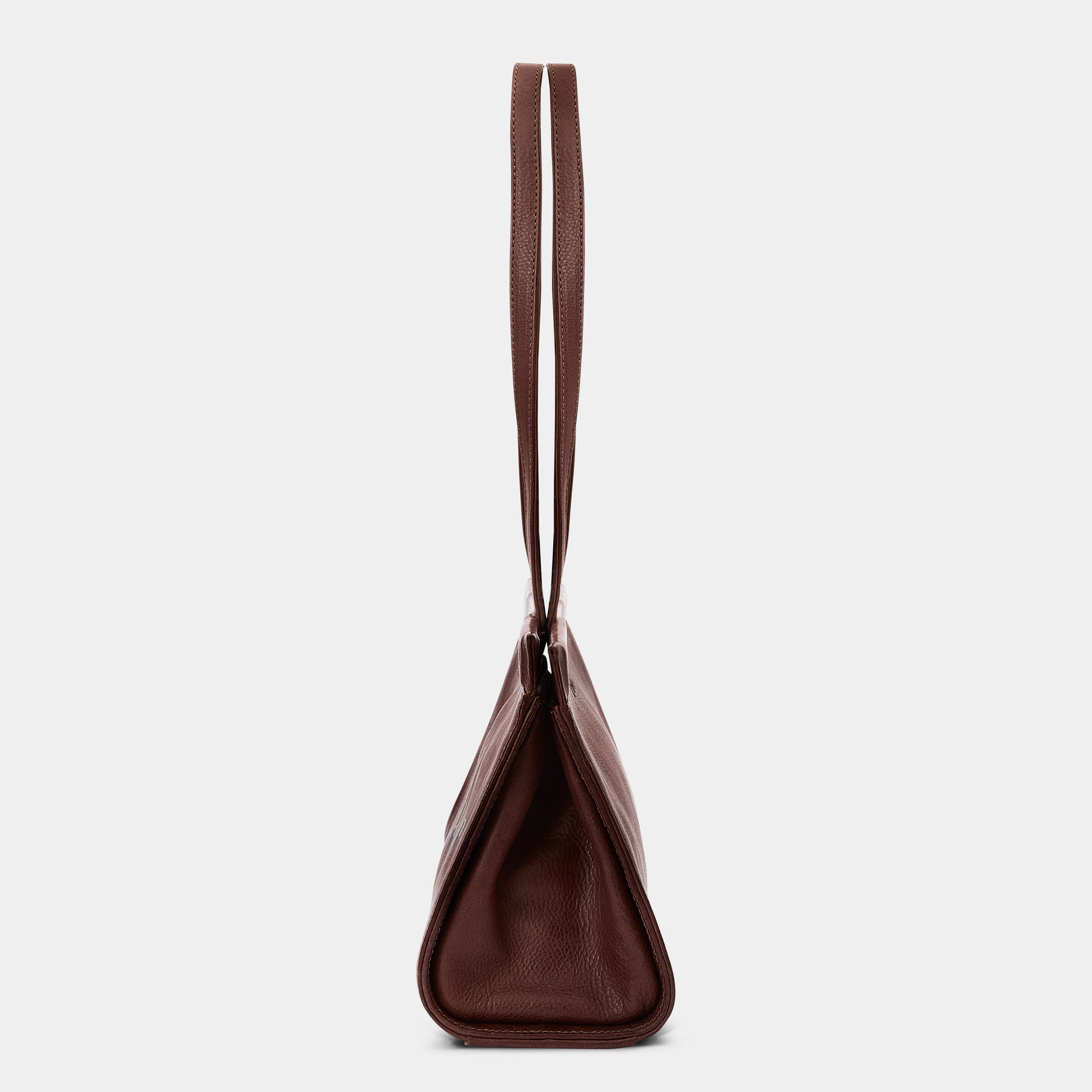 A dark brown leather shoulder bag shown from the back, featuring a single long strap and a structured triangular silhouette, set against a plain light gray background.