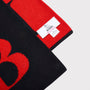 Close-up of a black knitted scarf with a bold red 'B', folded to show a white HADES brand label on the red side, against a light grey background.