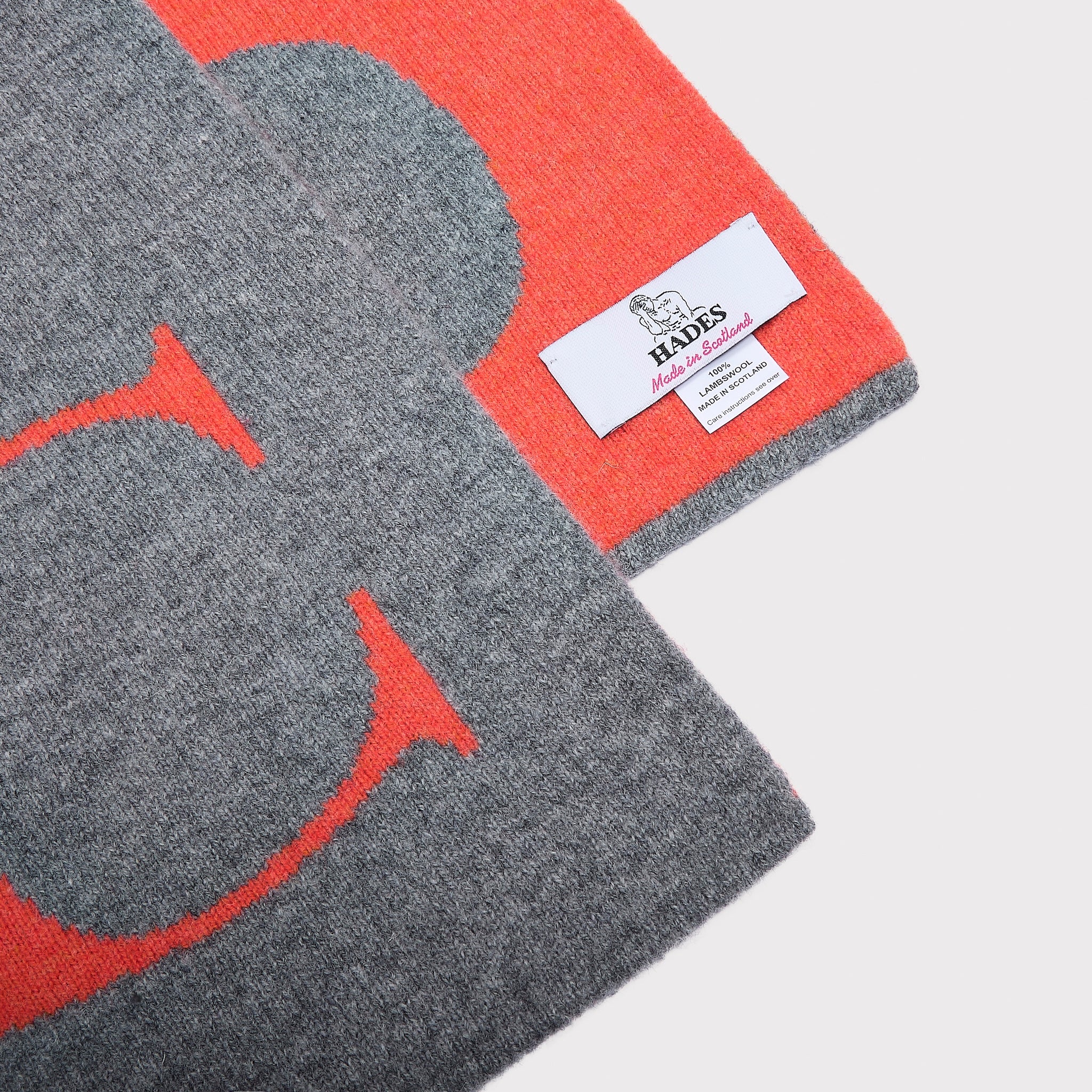 Close-up of a grey knit scarf with a large orange 'C' and a visible white 'HADES' label.