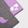 A close-up of a knitted scarf in grey and lavender purple, showing a white 'HADES - Made in Scotland' brand tag.
