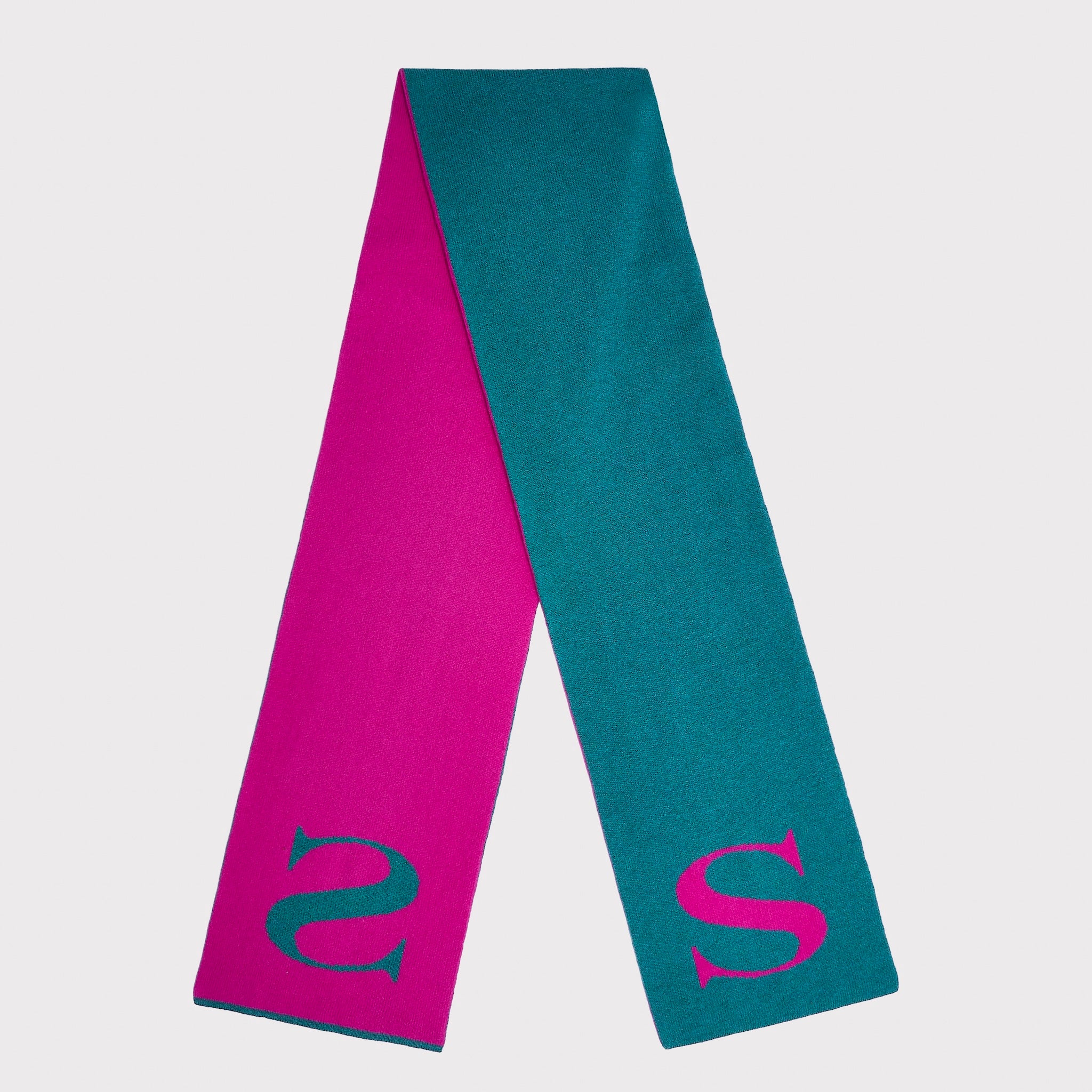 A double-sided knit scarf in vibrant pink and teal, featuring a stylised teal letter 'S' on one end and a matching pink 'S' on the other, displayed against a light grey background.
