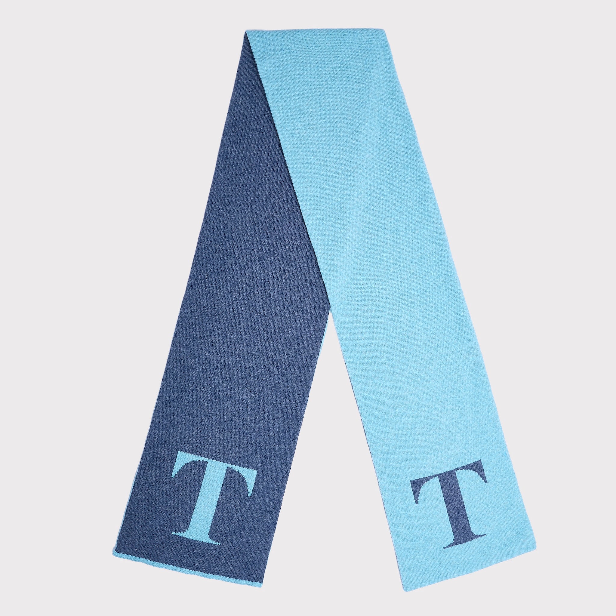 A double-sided knit scarf in navy blue and light blue, featuring a large capital letter 'T' on each end, displayed on a light gray background.