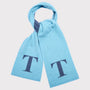 A light blue knit scarf with a dark navy blue double 'T' monogram printed on each end, shown against a neutral light grey background.