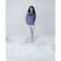 A model wearing the purple Albatross Knit from the Fleetwood Mac Collection, paired with white tights stood on a sofa. 