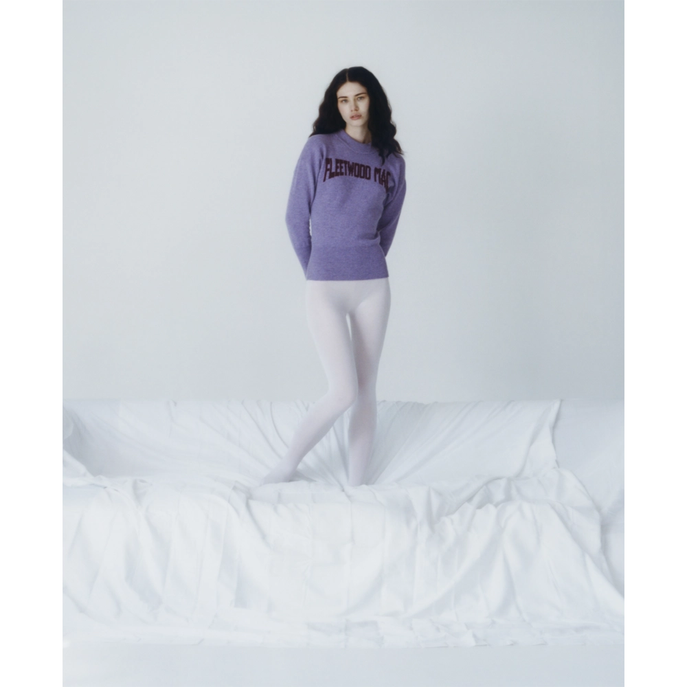 A model wearing the purple Albatross Knit from the Fleetwood Mac Collection, paired with white tights stood on a sofa. 
