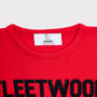 Close-up of the Fleetwood Mac bright red knit jumper with black lettering at the hem and a white neck label reading HADES Made in Scotland.