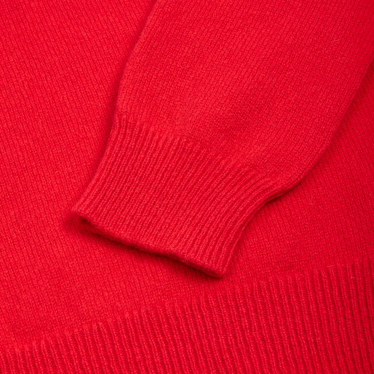 Close-up of the Fleetwood Mac bright red knit garment showing the ribbed cuff of a sleeve and matching ribbed fabric texture.