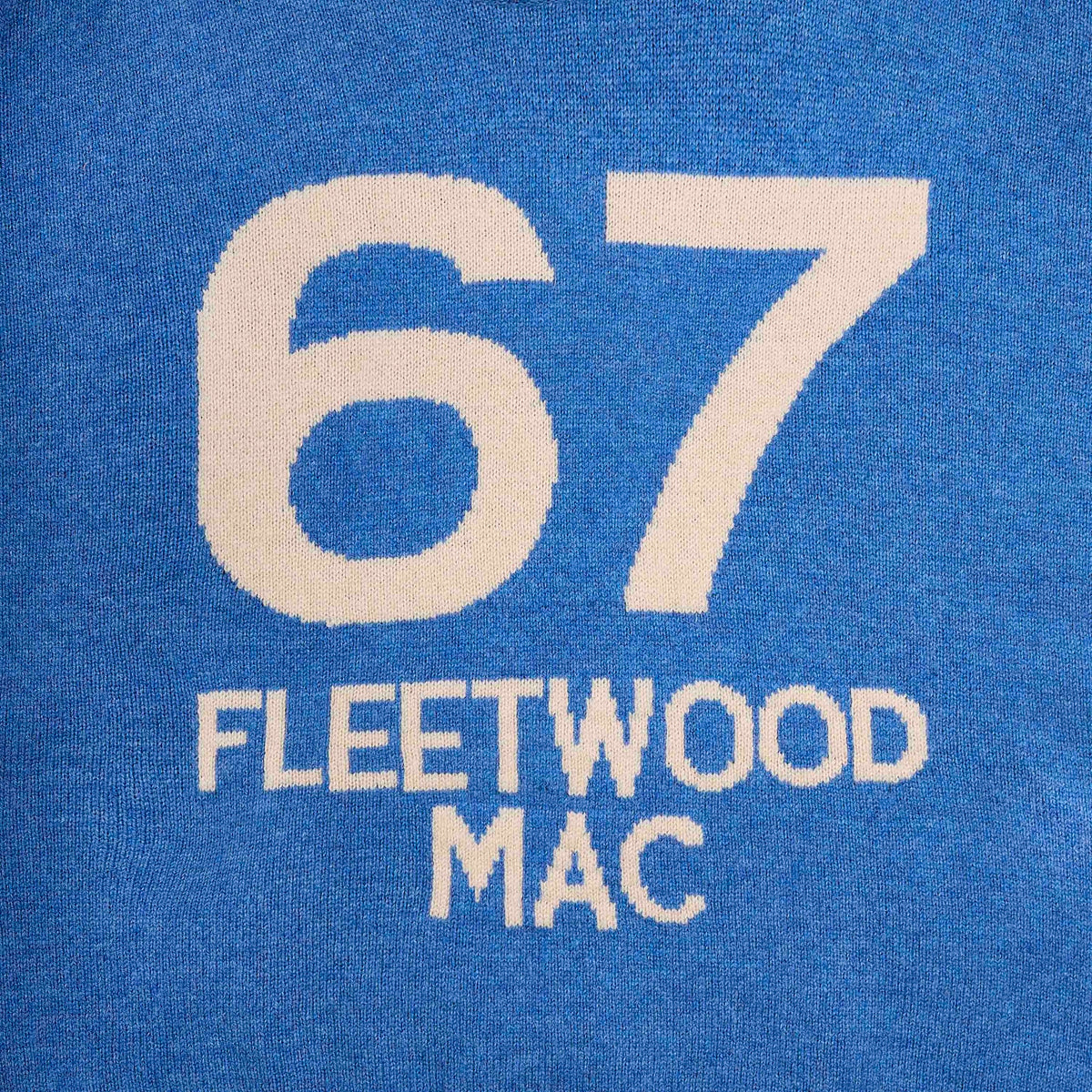 Close-up of a blue knit fabric with large cream-colored numbers '67' and the text 'FLEETWOOD MAC' knitted below.