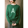 Person wearing a green sweater with a green letter 'A' on a plain background