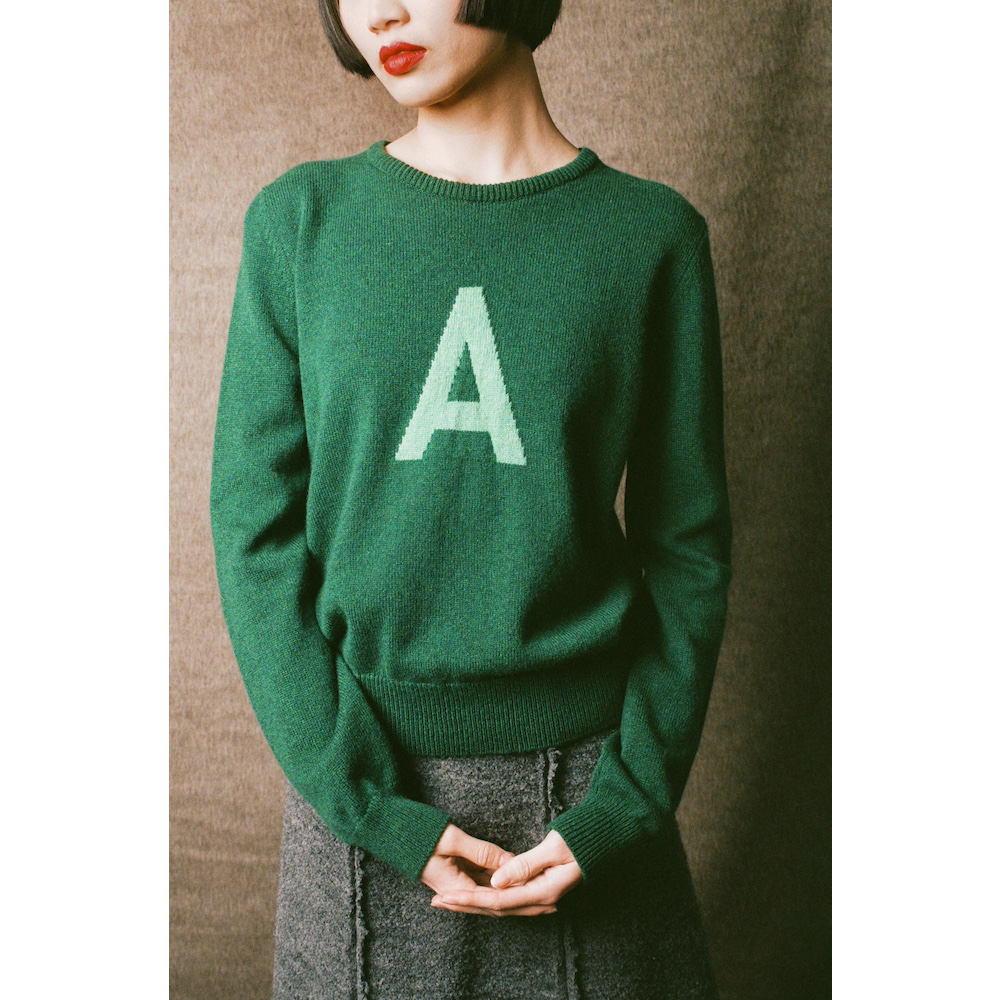 Person wearing a green sweater with a green letter 'A' on a plain background