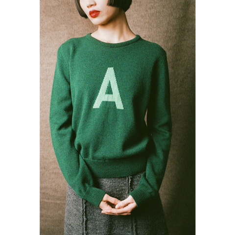 Person wearing a green sweater with a green letter 'A' on a plain background