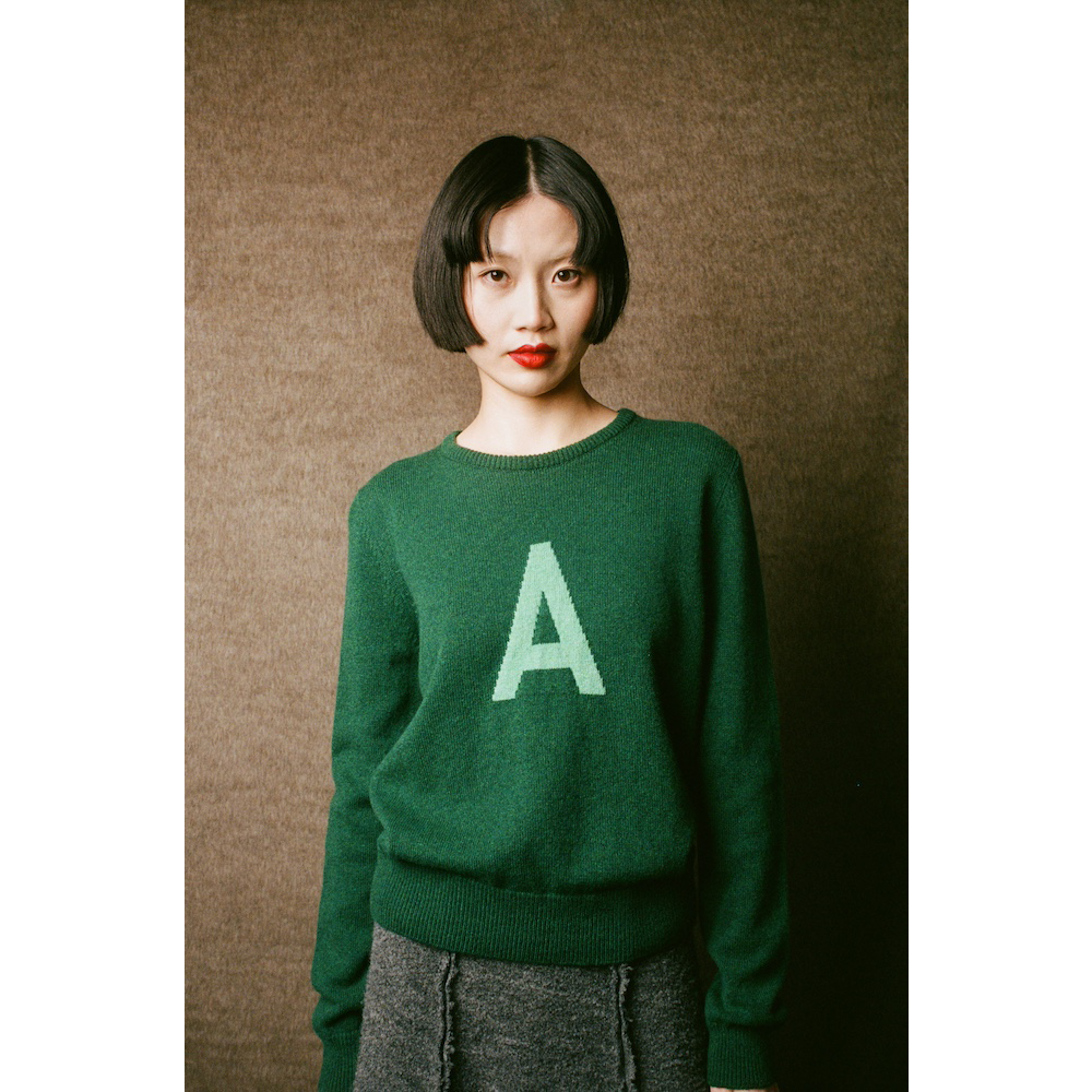 Person wearing a green sweater with a letter 'A' on a brown background