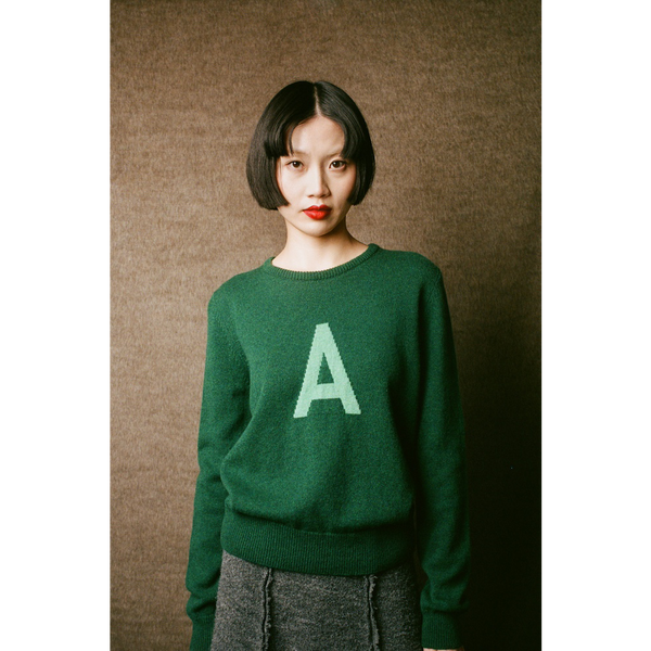 Person wearing a green sweater with a letter 'A' on a brown background