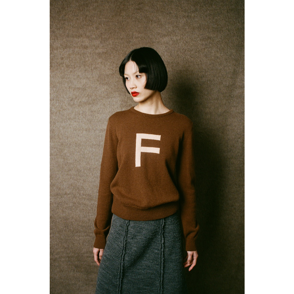 Person wearing a brown sweater with a white 'F' on a plain background