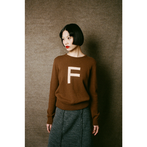 Person wearing a brown sweater with a white 'F' on a plain background