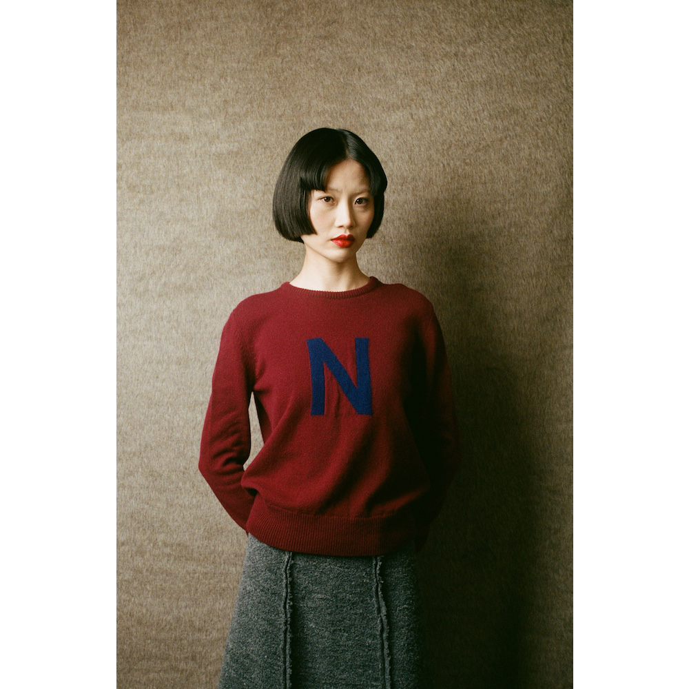HADES model wearing burgundy jumper with a blue letter 'N' 