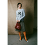 Woman holding a red handbag with an 'E' on a textured wall background