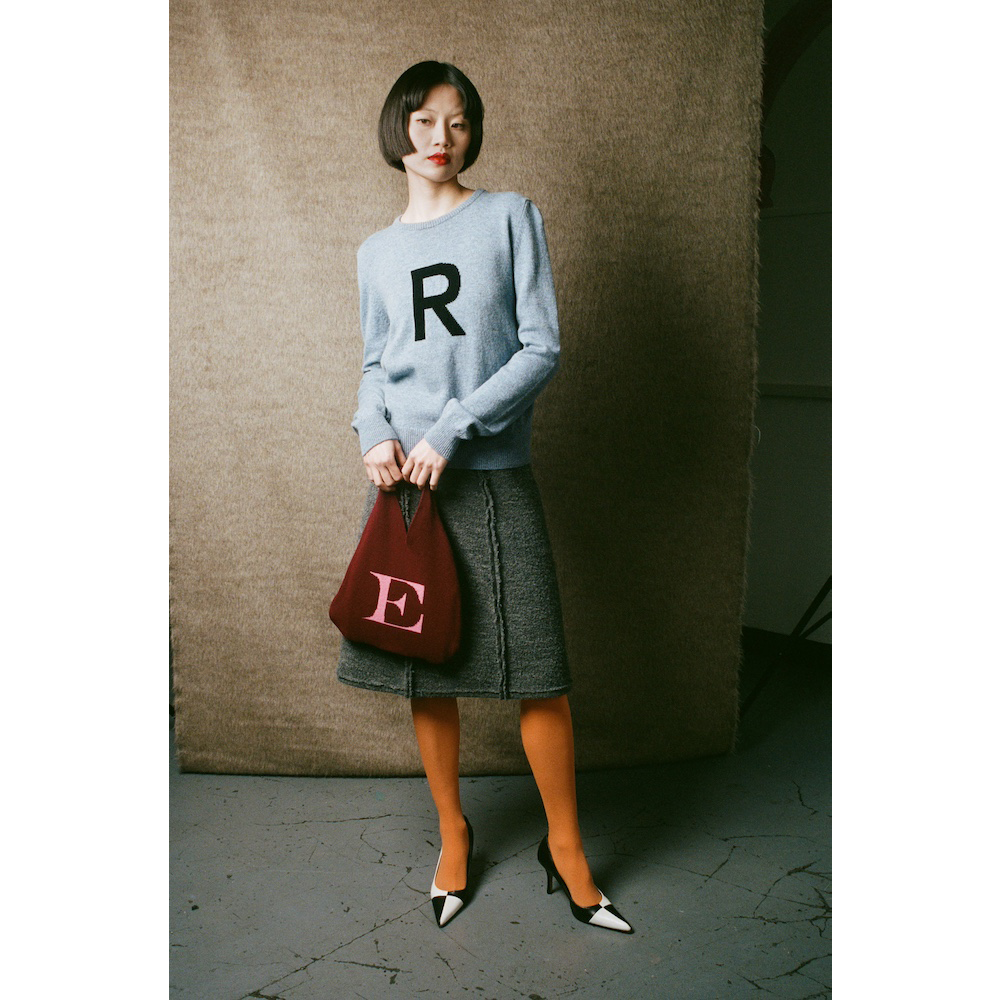 Woman holding a red handbag with an 'E' on a textured wall background