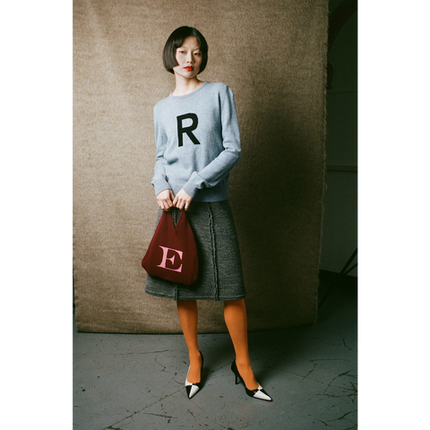 Woman holding a red handbag with an 'E' on a textured wall background