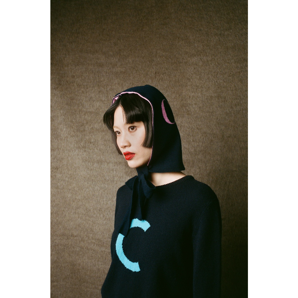 Person wearing HADES Navy blue knit  with a turquoise letter 'C' 