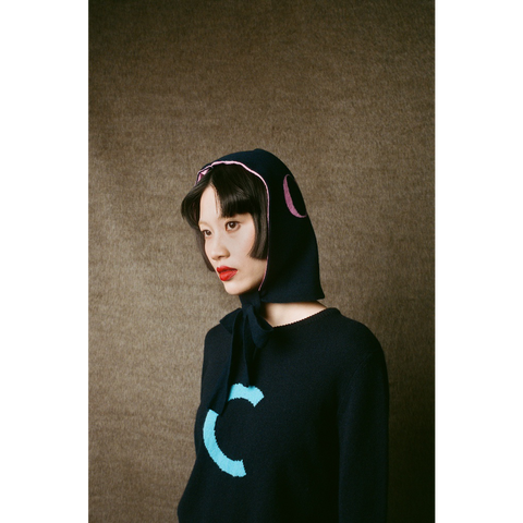 Person wearing HADES Navy blue knit  with a turquoise letter 'C' 