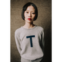 Woman wearing a gray sweater with a blue 'T' on a textured brown background