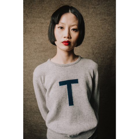 Woman wearing a gray sweater with a blue 'T' on a textured brown background