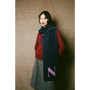 Woman wearing the HADES red 'N' Alphabet knit jumper, grey 'Inside Out' skirt, and dark blue scarf with a purple 'N' against a wall
