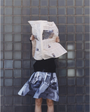 An image of a model wearing the Egos Arcady Skirt, holding a newspaper in front of her face. 