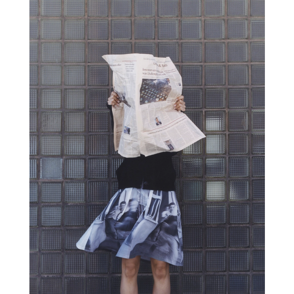 An image of a model wearing the Egos Arcady Skirt, holding a newspaper in front of her face. 