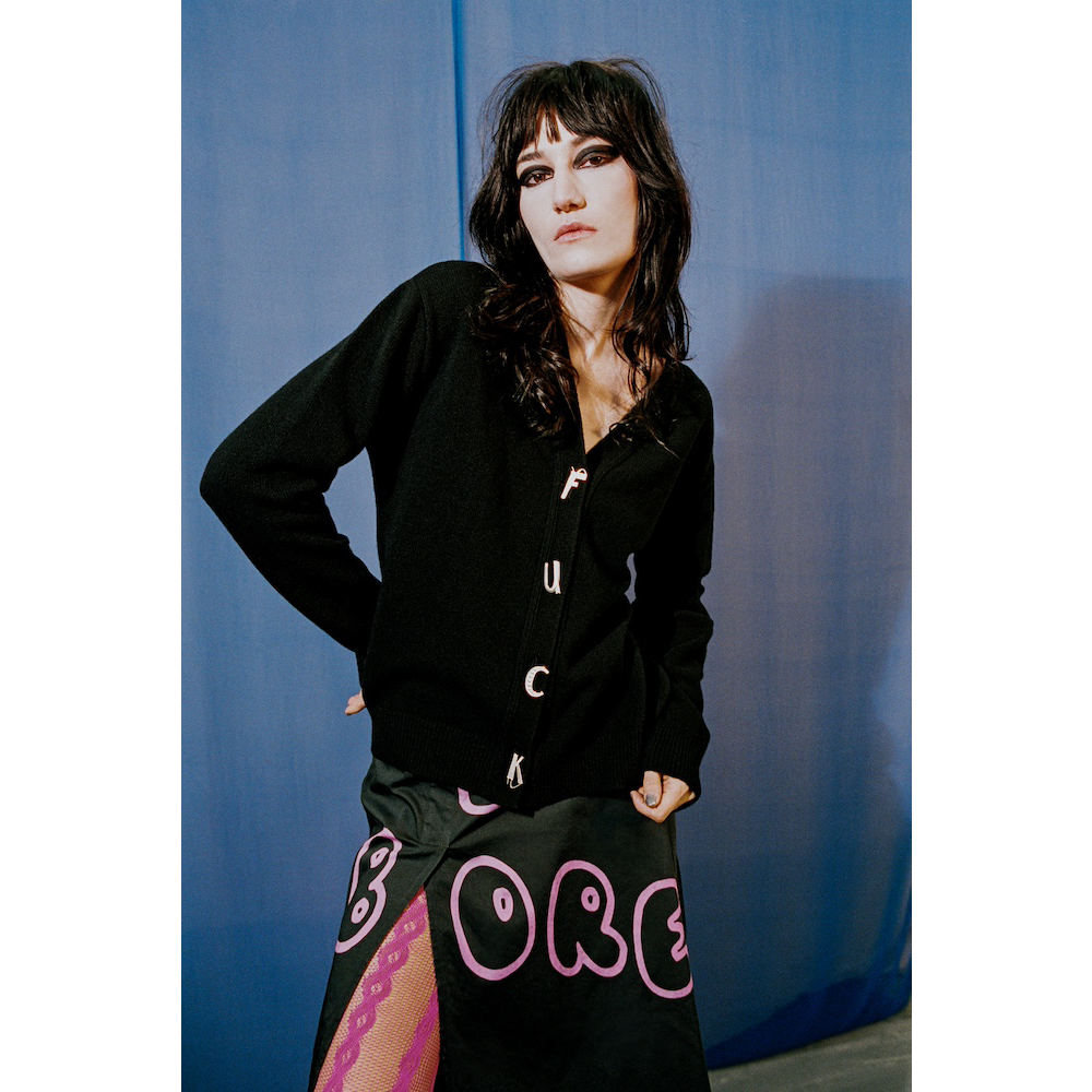 Person wearing a black cardigan and colourful skirt with 'BORED' text against a blue background