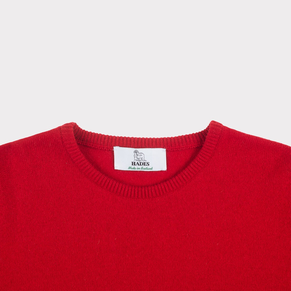 Close-up of a bright red crewneck jumper showing the inner neck label which reads 'HADES Made in Scotland'.