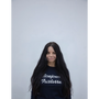 Artist Gillian Wearing, wearing a dark navy sweatshirt with 'Bonjour Tristresse' printed in white script across the chest, set against a plain light grey background.