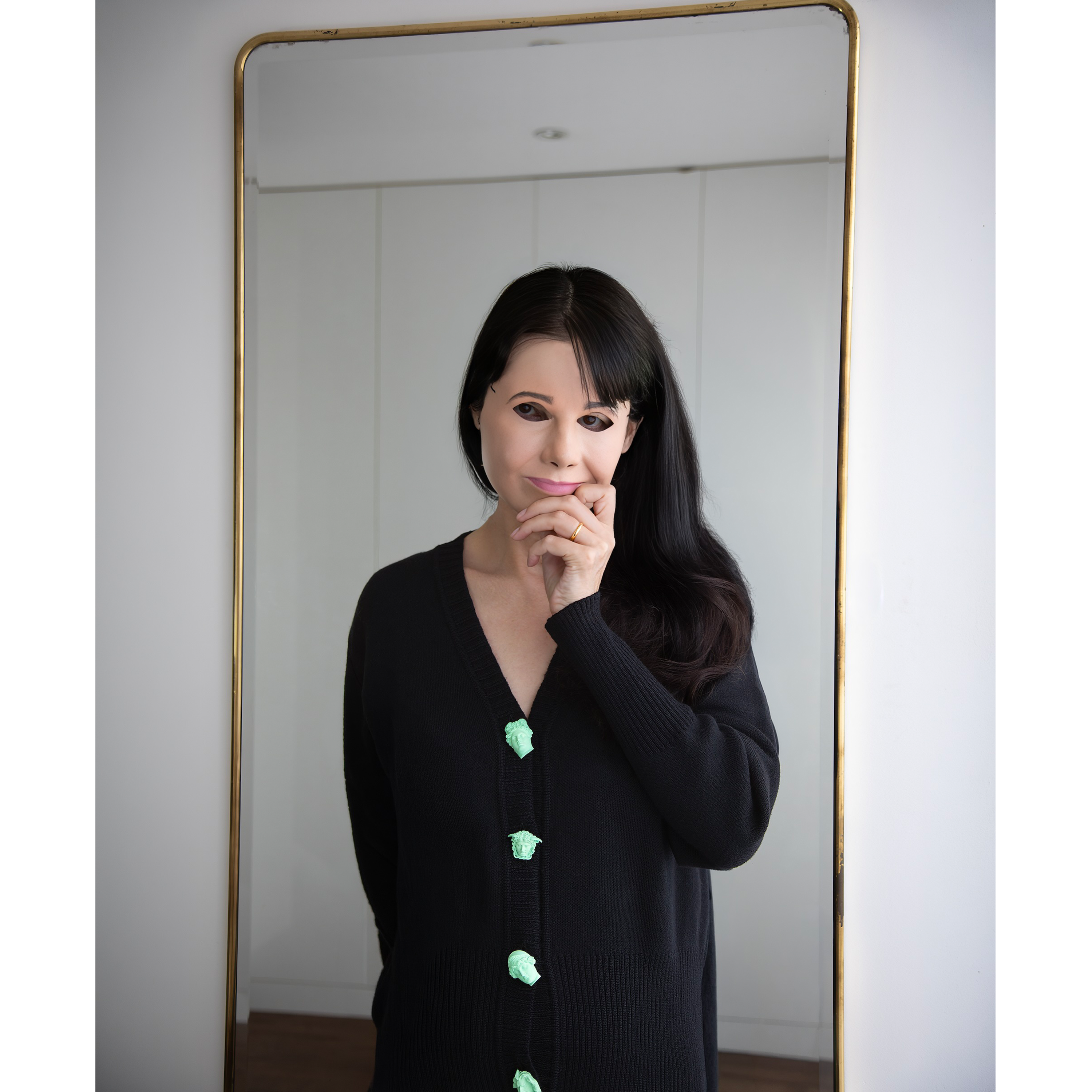 Artist Gillian Wearing wearing the Greek Mythology Cardigan, in front of a mirror wearing a mask to cover her face.