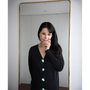 Artist Gillian Wearing wearing the Greek Mythology Cardigan, in front of a mirror wearing a mask to cover her face.