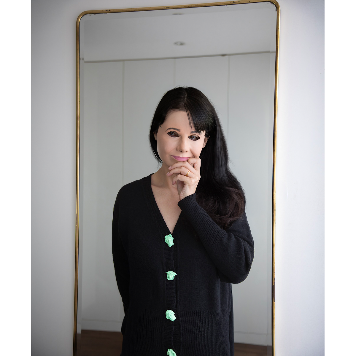 Artist Gillian Wearing wearing the Greek Mythology Cardigan, in front of a mirror wearing a mask to cover her face.